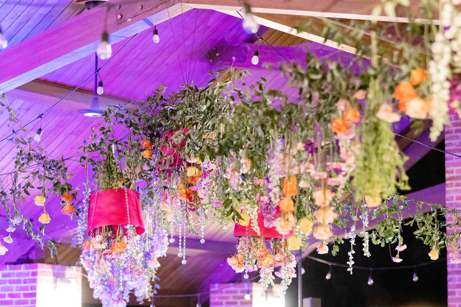 A hanging floral installation glows under purple uplighting