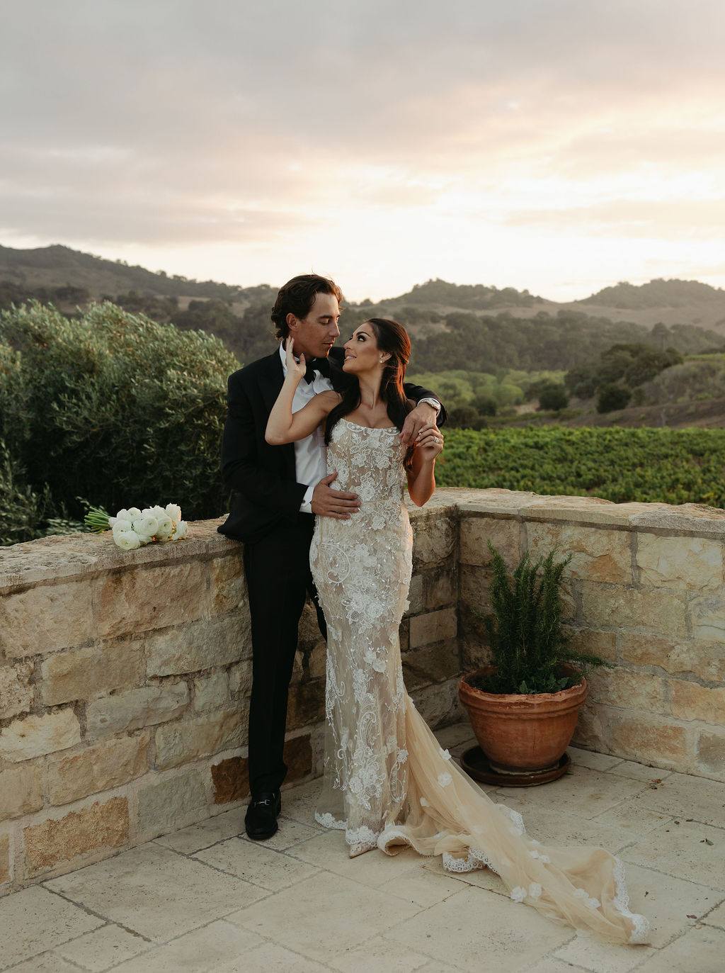 A couple embraces against a sunlit stone estate wall