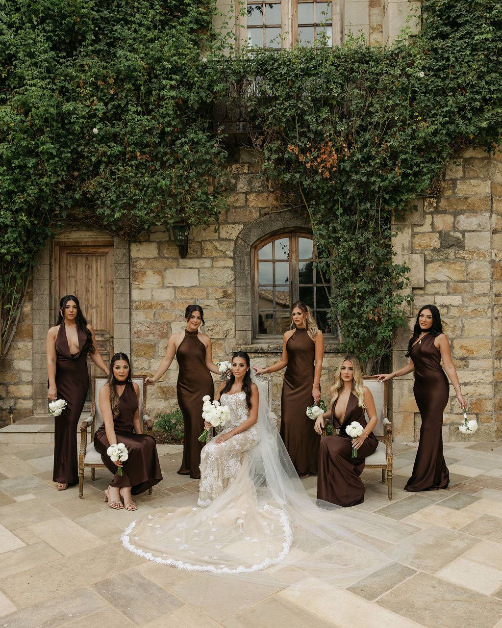 Bridesmaids in chocolate brown gowns before a stone estate