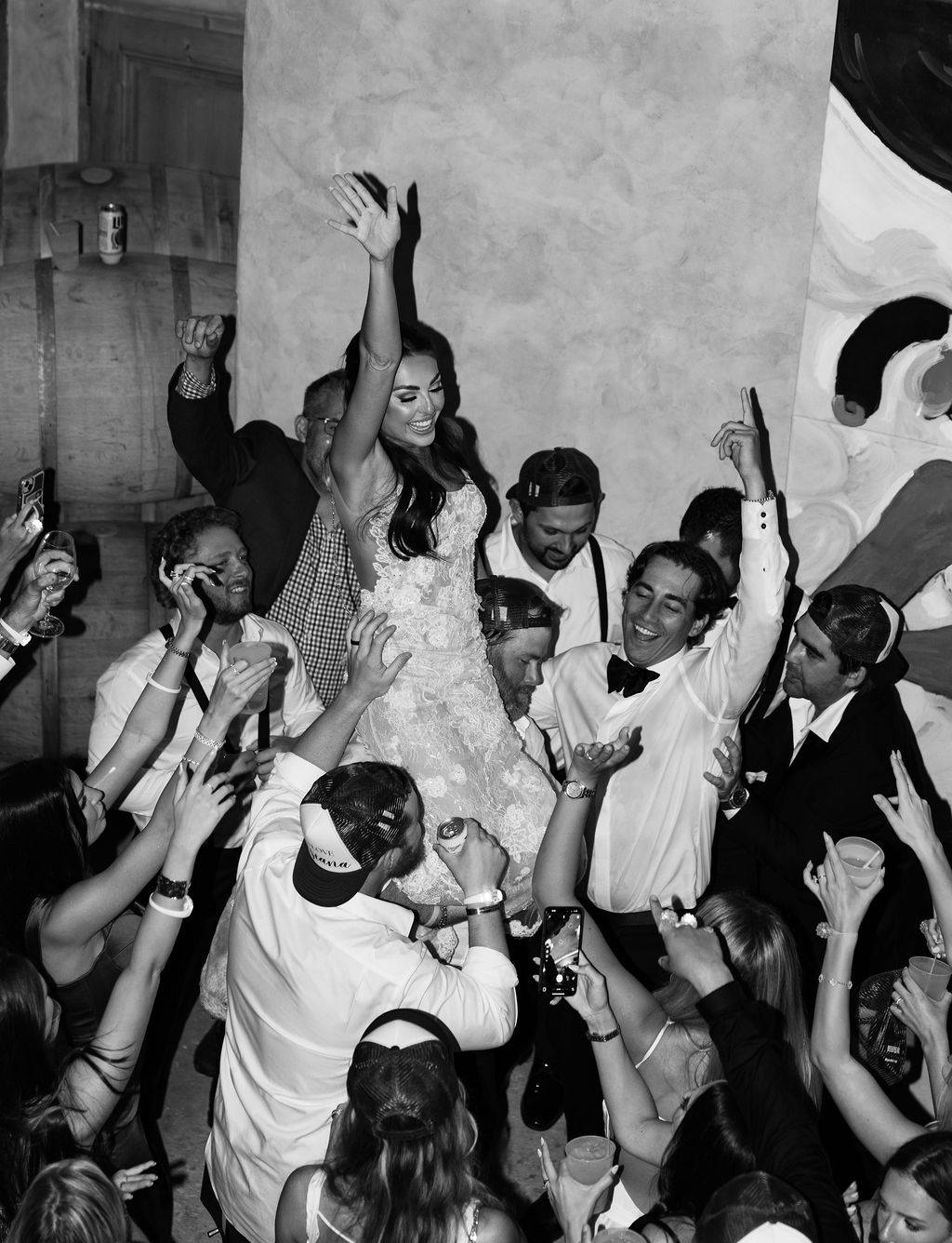 Guests cheer as the bride is lifted on the dance floor, black and white