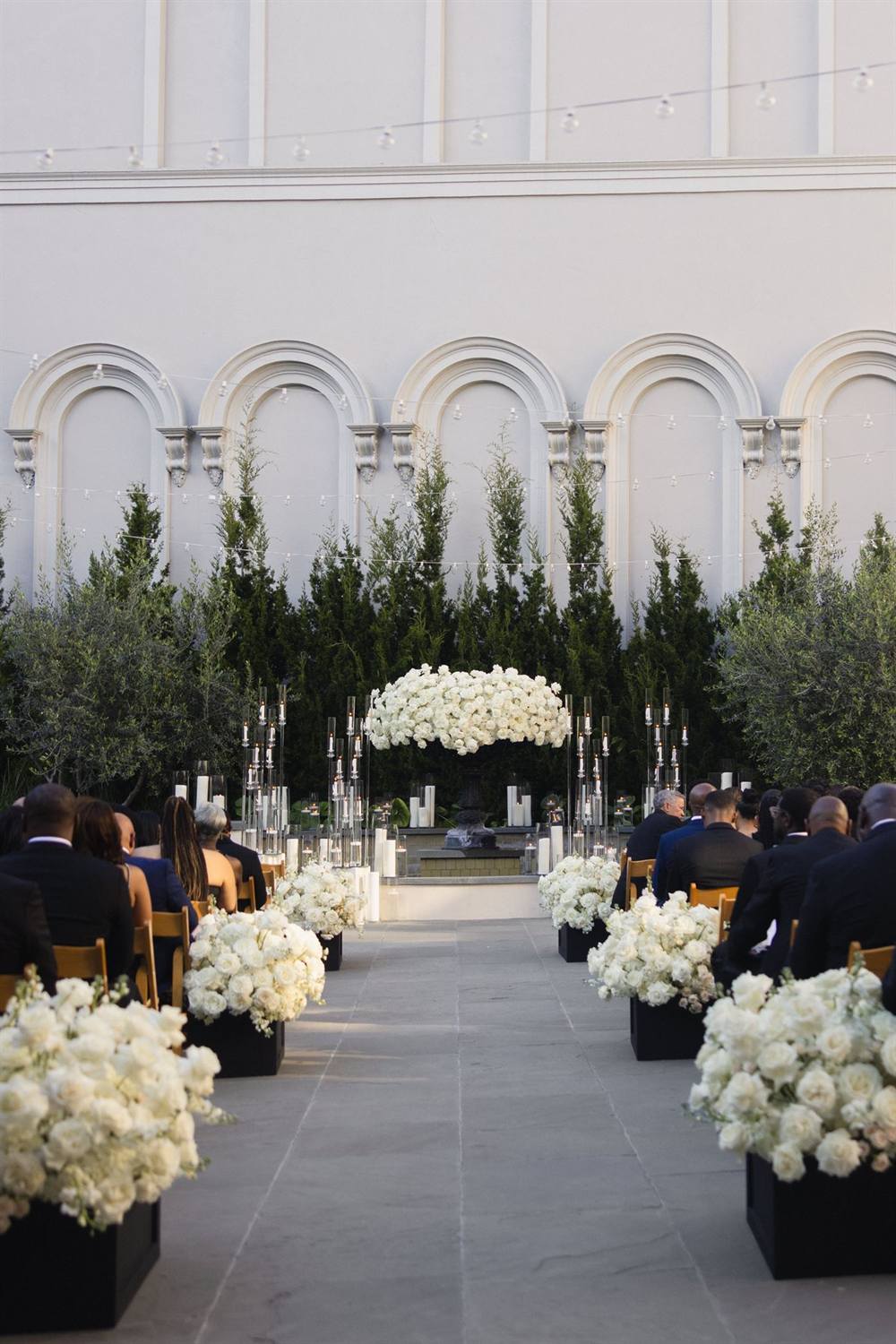 Guests fill a ceremony aisle lined with glass floral stands