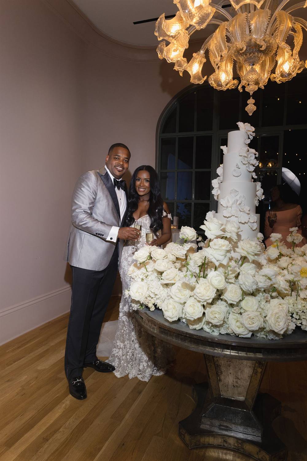 The couple beside a towering all-white wedding cake